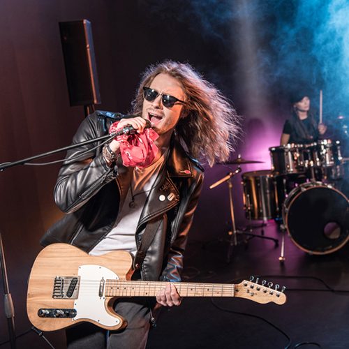 Male singer with microphone and rock and roll band performing hard rock music on stage